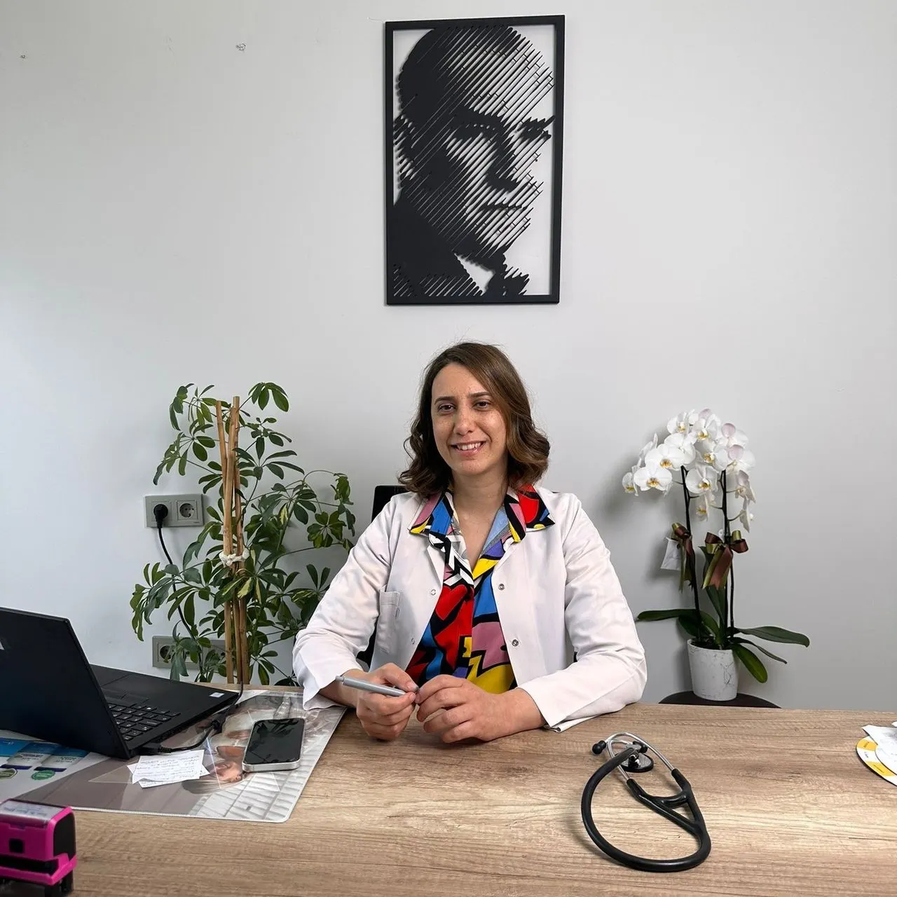 Uzm. Dr. Selen Şipal muayenehanesinde, masasında gülümsüyor